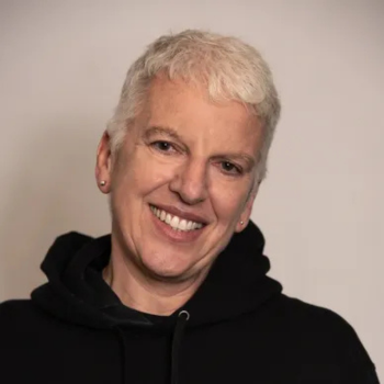 Portrait of a smiling person with short grey hair wearing a black hoodie.
